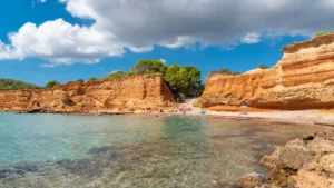 Sa Caleta en Ibiza con arena rojiza, acantilados y mar tranquilo.