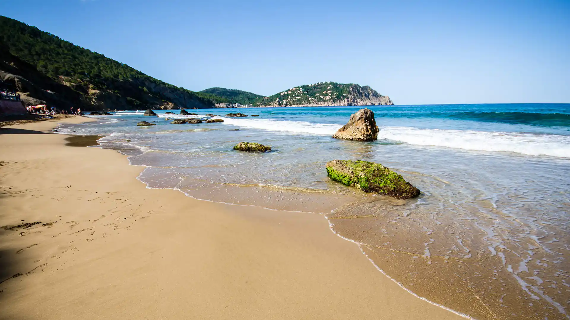 Playa de Aigües Blanques en Ibiza con arena clara, rocas y oleaje suave