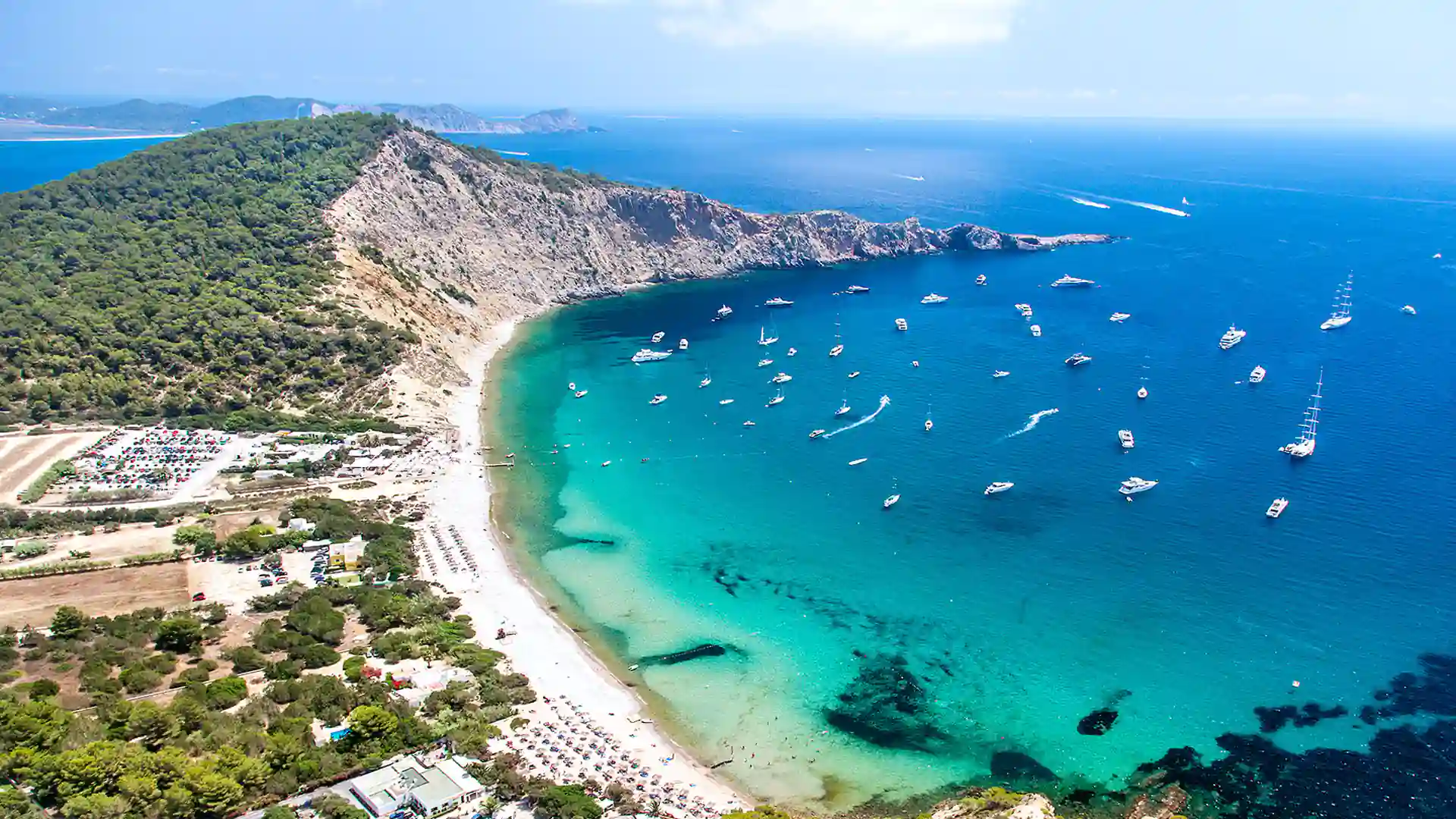 Vista aérea de Cala d’Hort en Ibiza con playa, acantilados y barcos fondeados en aguas claras