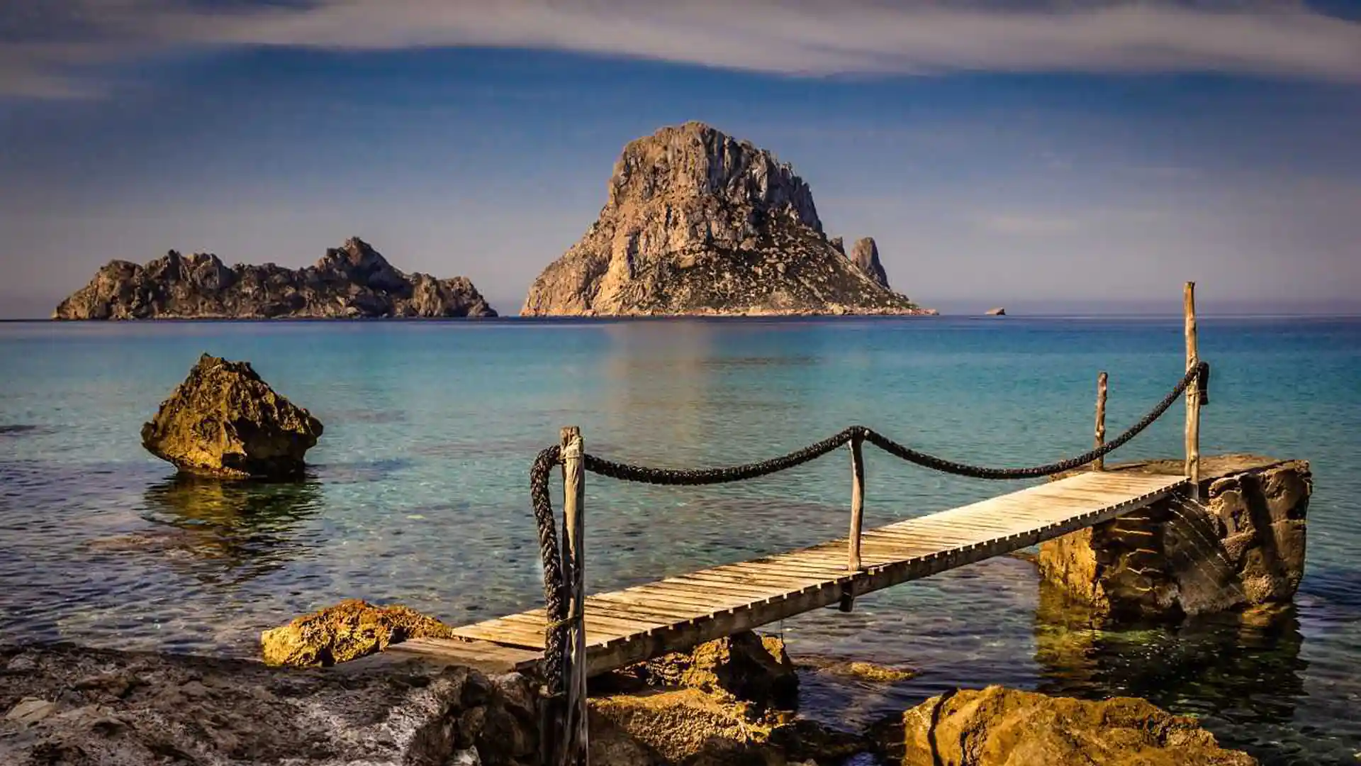 Muelle de madera frente a Es Vedrà en la costa sur de Ibiza, con aguas tranquilas y fondo claro