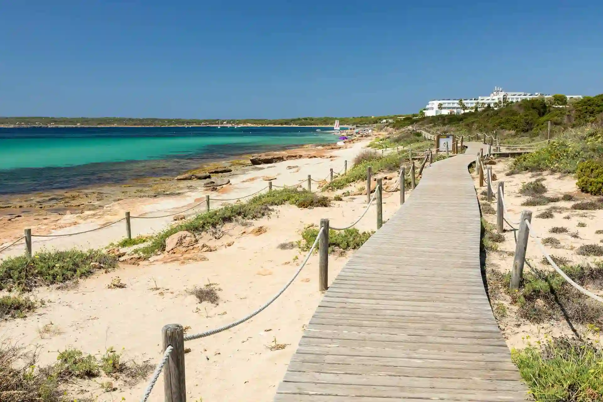 Pasarela de madera junto a una playa tranquila de Formentera con aguas turquesas y paisaje mediterráneo